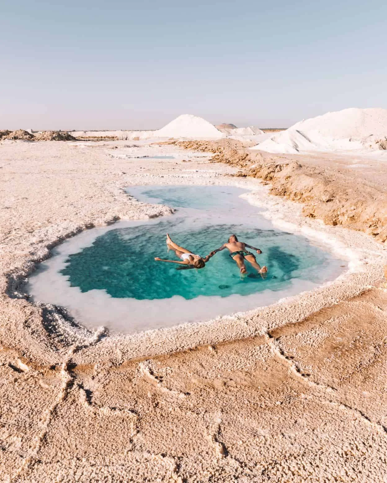 A person floating effortlessly on the surface of a Siwa salt lake under a clear blue sky