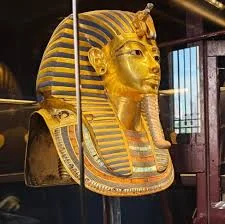 The gold funerary mask of Tutankhamun displayed under amber museum lighting at the Grand Egyptian Museum
